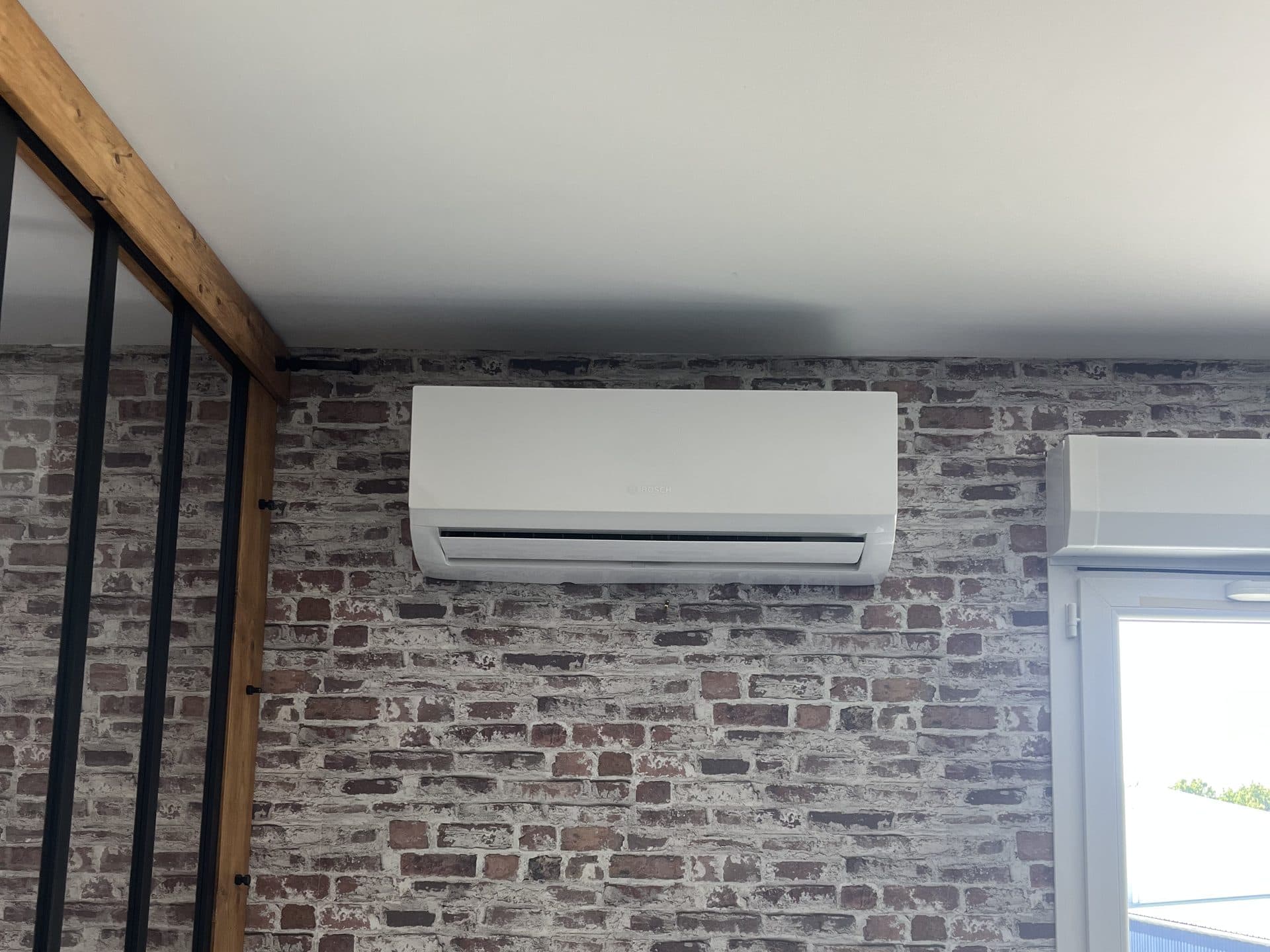 Unité intérieure de climatisation posée sur un mur de brique, près d'une verrière d'atelier