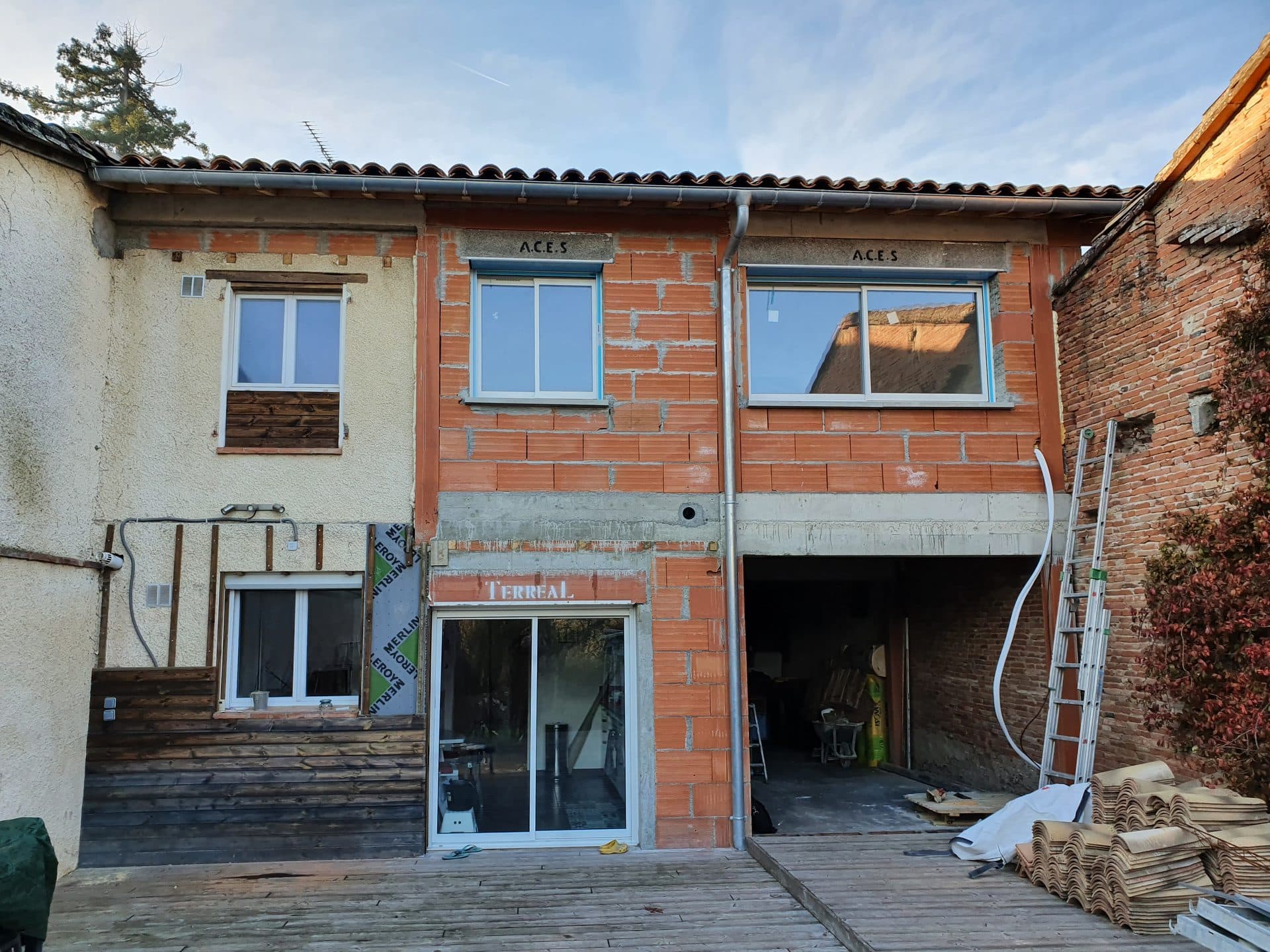 Extension en brique montée contre une maison existante, linteaux marqués A.C.E.S