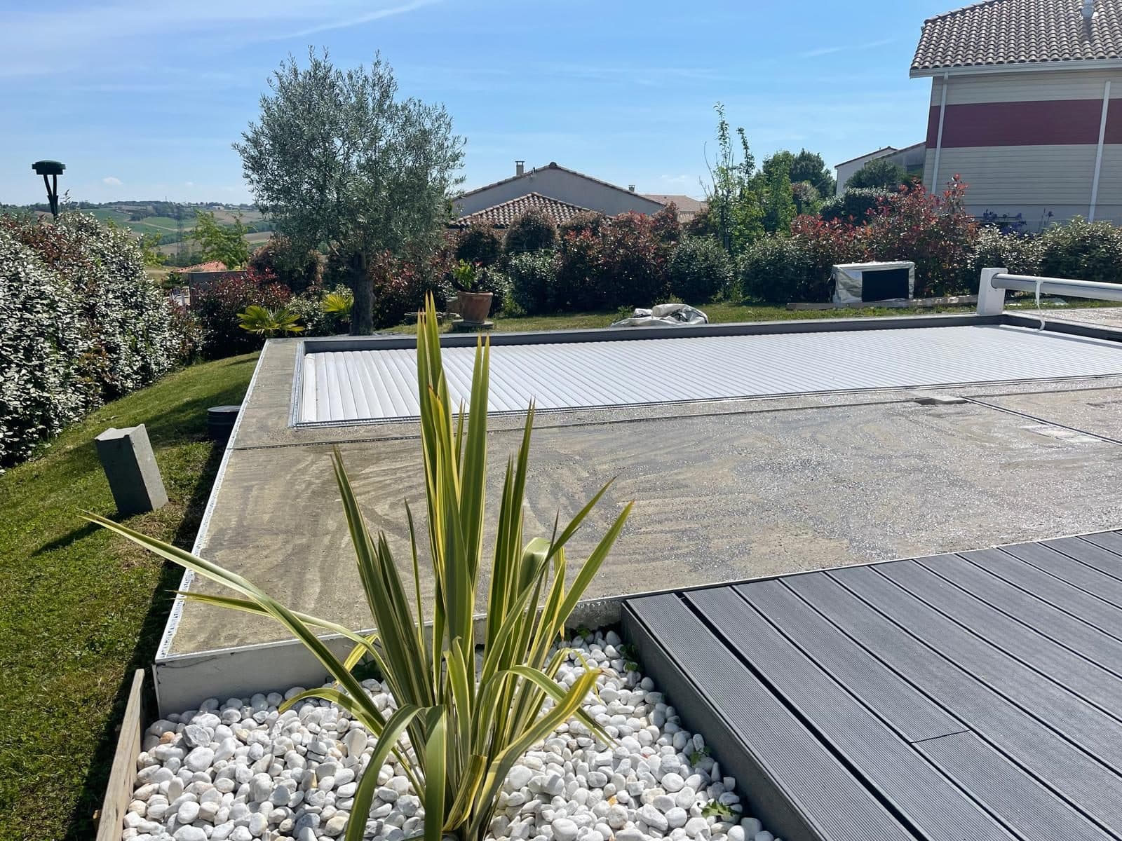 Piscine équipée d'un volet roulant, terrasse bois et plage minérale