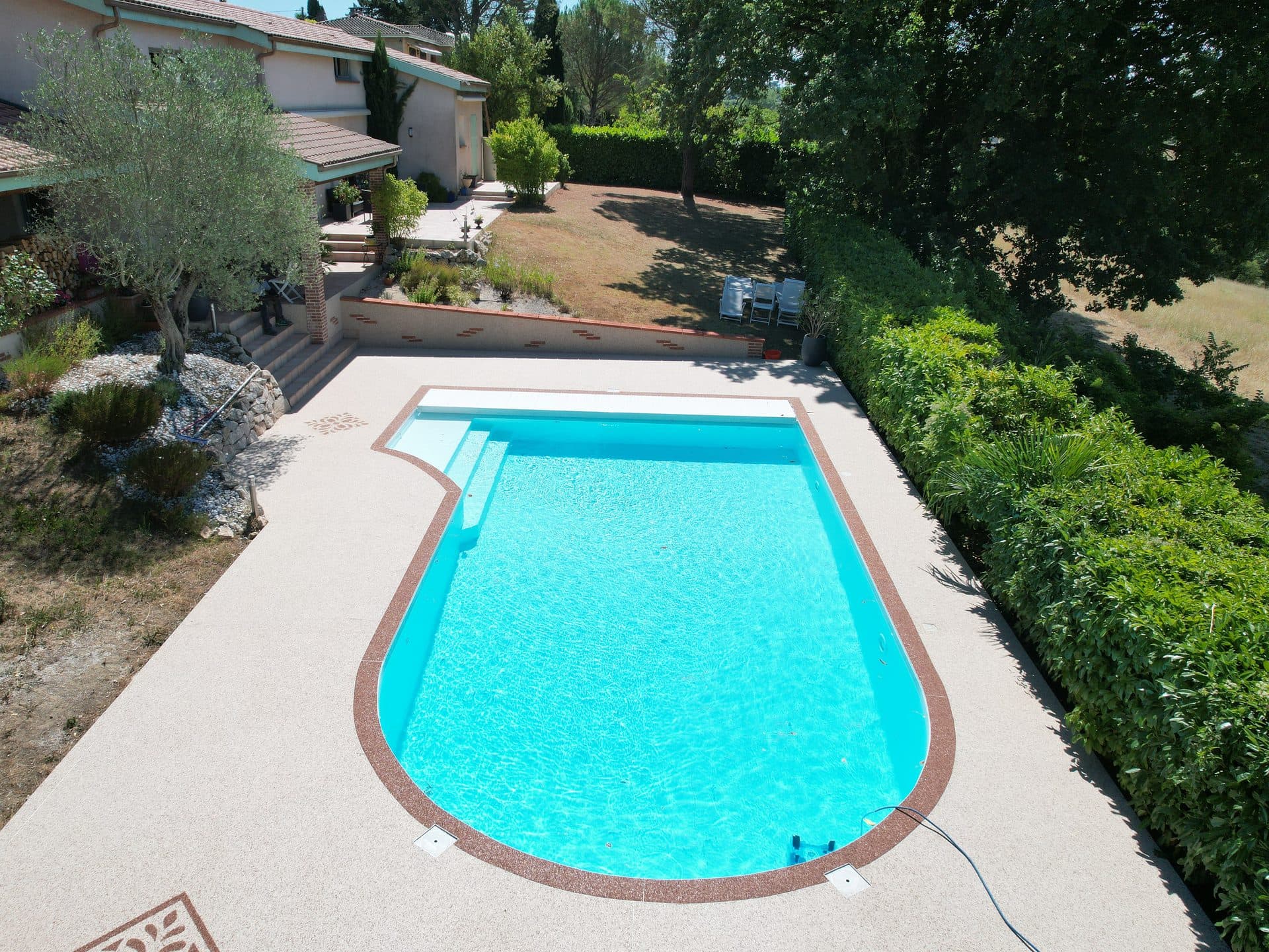 Vue aérienne d'une piscine maçonnée et de sa plage en moquette de pierre