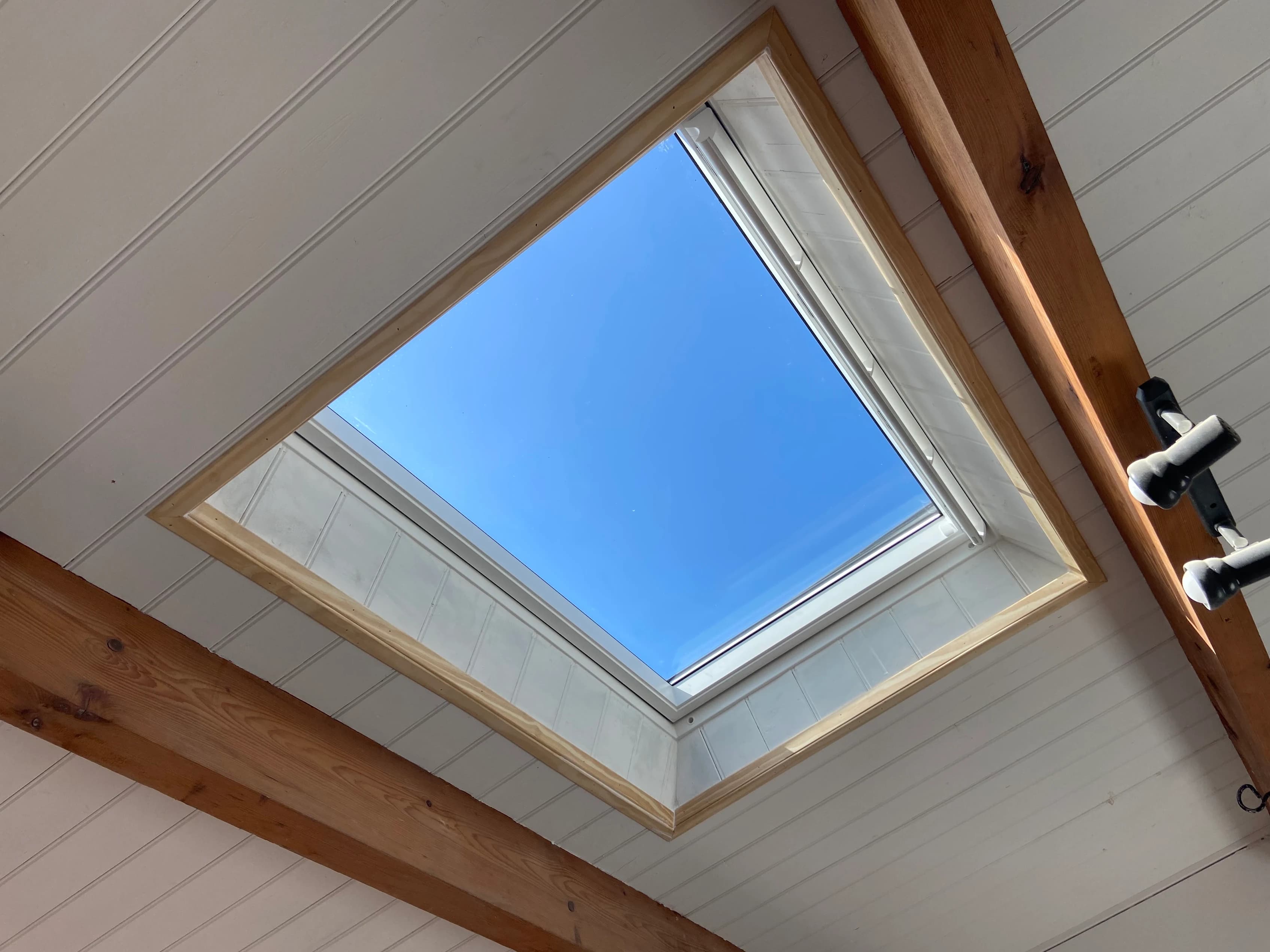 Fenêtre de toit ouverte sur ciel bleu entre poutres apparentes